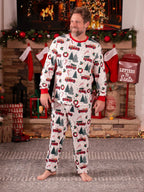 Smiling man wearing a white long-sleeve Christmas pajama set with vintage red truck and tree patterns by a fireplace.
