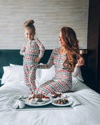 Mother and young daughter wearing matching white Fair Isle Christmas sleepwear enjoying a breakfast tray with waffles and coffee on a white bed.