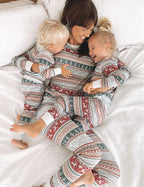 Mother laughing on bed with two toddlers wearing matching grey Fair Isle holiday pajama sets.