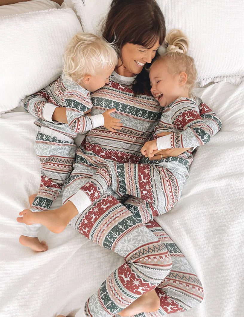 Mother laughing on bed with two toddlers wearing matching grey Fair Isle holiday pajama sets.