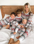 Mother and three children sitting on bed in matching grey Fair Isle reindeer Christmas pajamas with white cuffs.