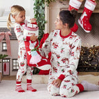 Mother and young daughter kneeling near a fireplace while holding a red personalized Christmas stocking in matching holiday pajamas.