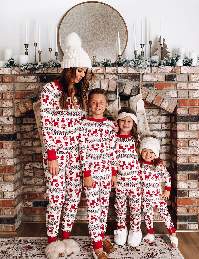 Mother and three children standing together in front of a brick fireplace wearing matching red and white Fair Isle reindeer pajama sets