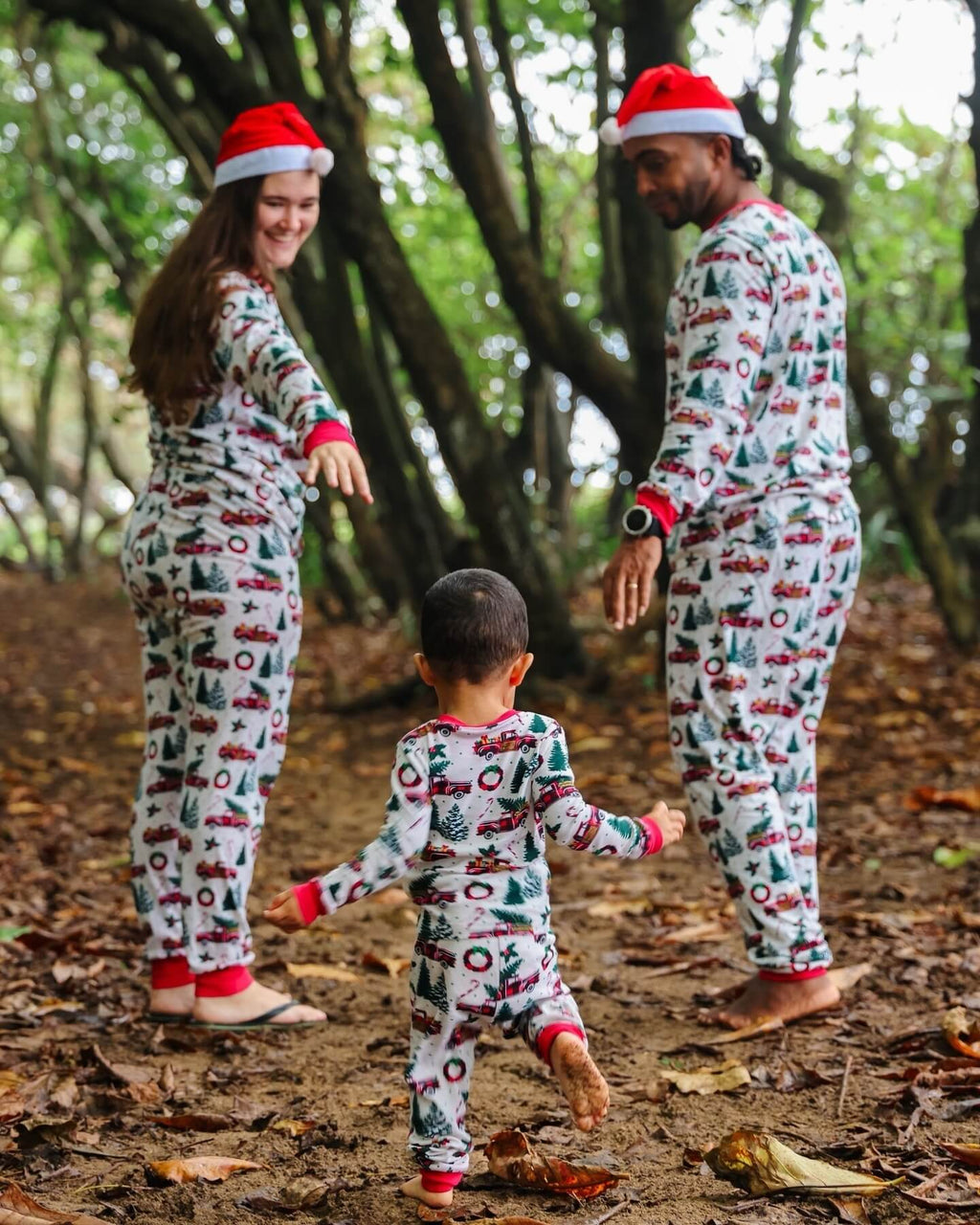 Parents and toddler walking along a wooded dirt path in matching white and red truck print Christmas long-sleeve pajama sets.