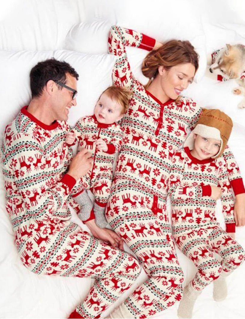 Overhead top-down photo of a family of four and their small dog lying together on a white bed in matching red reindeer Fair Isle pajamas.