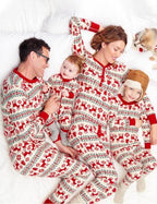 Overhead top-down photo of a family of four and their small dog lying together on a white bed in matching red reindeer Fair Isle pajamas.