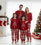 Family of four in red matching Christmas pajamas with tree, reindeer and polar bear prints by a decorated tree