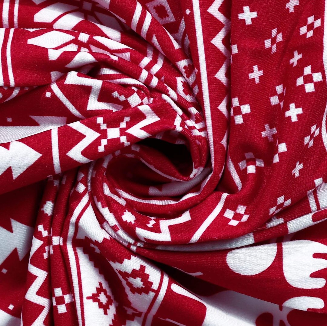 Macro close-up view of swirled soft red fabric showing the detailed white Nordic Fair Isle pattern with printed pine trees, snowflakes, and geometric shapes.