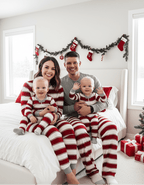 Parents sitting on a white bed with twin babies wearing matching red and white candy cane striped holiday lounge sets.