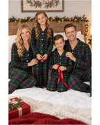 Family in dark green tartan pajamas holding a red ribbon on a bed.
