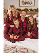 Family of four sitting together on a bed in red and blue plaid pajamas.
