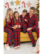 Family in red and blue plaid pajamas seated on a yellow sofa with a wrapped gift.