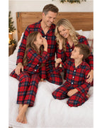 Family seated on a bed wearing matching red and blue plaid pajamas.