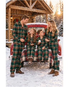 Family in light green tartan pajamas posing together beside a red truck in a snowy cabin setting.