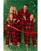 Family in red and black plaid pajamas holding a red ribbon against a green confetti backdrop.