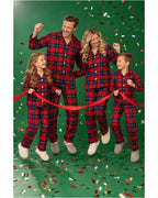 Family wearing red and blue plaid pajamas with a red ribbon and confetti against a green backdrop.