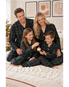 Family seated together on a textured bedspread wearing matching dark green tartan pajamas.