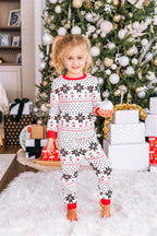 Little girl holding a silver ornament wearing kids' white Fair Isle snowflake Christmas pajamas in front of gifts.