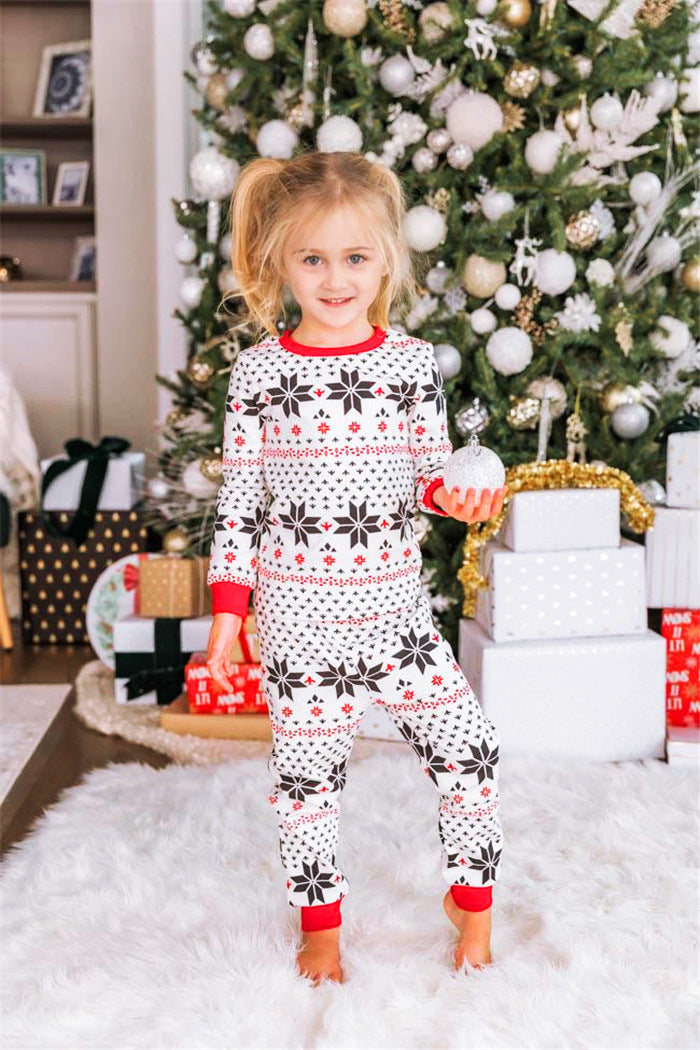 Little girl holding a silver ornament wearing kids' white Fair Isle snowflake Christmas pajamas in front of gifts.