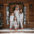 Family of five posing on a snowy cabin porch surrounded by evergreen garland, dressed in matching white pajamas with red truck and wreath print.