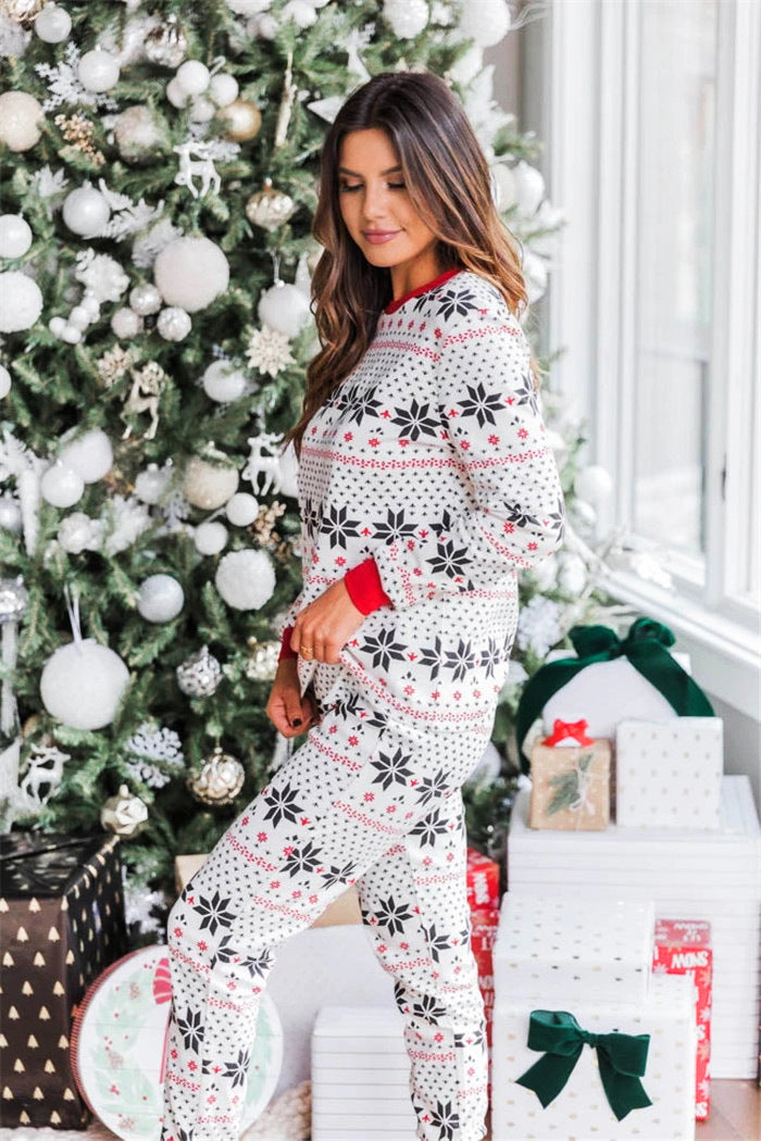 Side profile view of a woman wearing white and red Fair Isle snowflake holiday sleepwear next to decorated gifts.