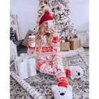 Smiling woman taking a standing mirror selfie in a cozy bedroom, holding a festive mug and modeling a two-piece red and white Fair Isle reindeer holiday pajama set.