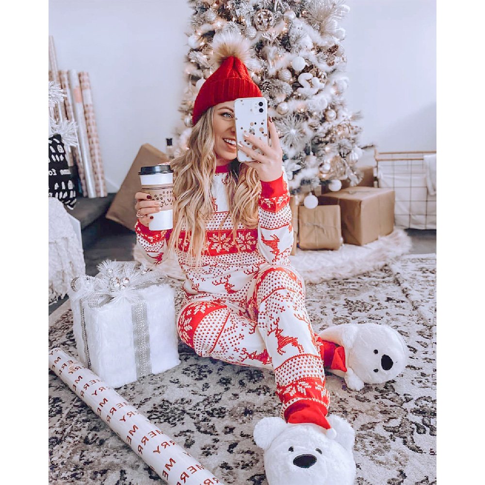 Smiling woman taking a standing mirror selfie in a cozy bedroom, holding a festive mug and modeling a two-piece red and white Fair Isle reindeer holiday pajama set.