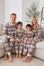 Parents and two boys sitting on a cream sofa in grey Christmas pajamas with red reindeer bands and green tree rows.