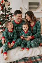 Family sitting together beside a Christmas tree in green Fair Isle pajamas, with a baby on mother's lap.