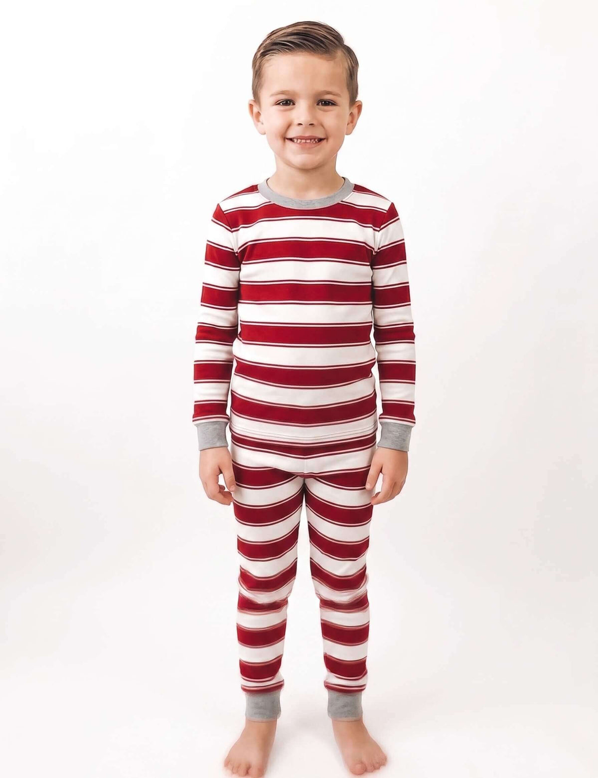 Boy modeling red and white striped Christmas pajamas with grey cuffs against a white background.