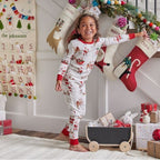 Smiling girl in long-sleeve white Santa print pajamas reaching for a stocking hanging on the wall near a Christmas countdown calendar.